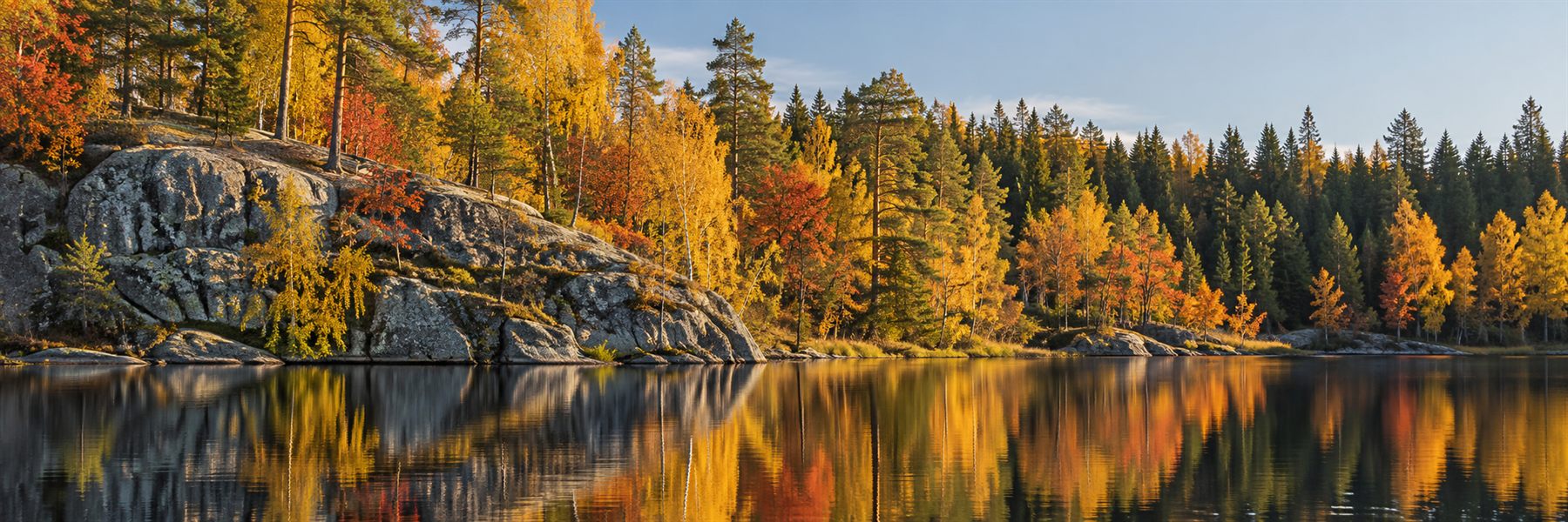 Granitklippa och höstskog i gult och rostrött som speglar sig i en stilla sjö.